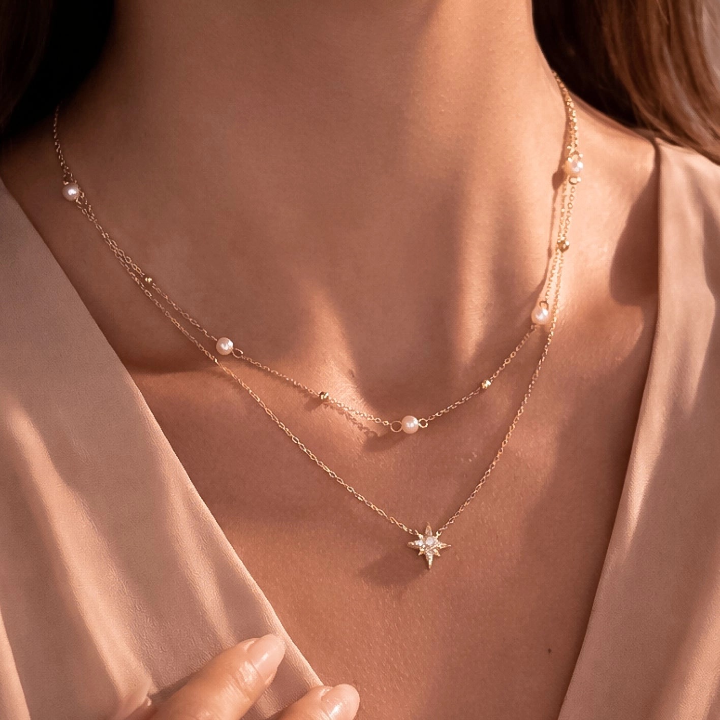 Layered fine gold chains with pearl stations and a starburst pendant worn in soft daylight